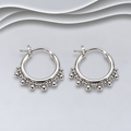 Pair of polished sterling silver hoop earrings with beaded detailing along the lower edge and hinged fastenings